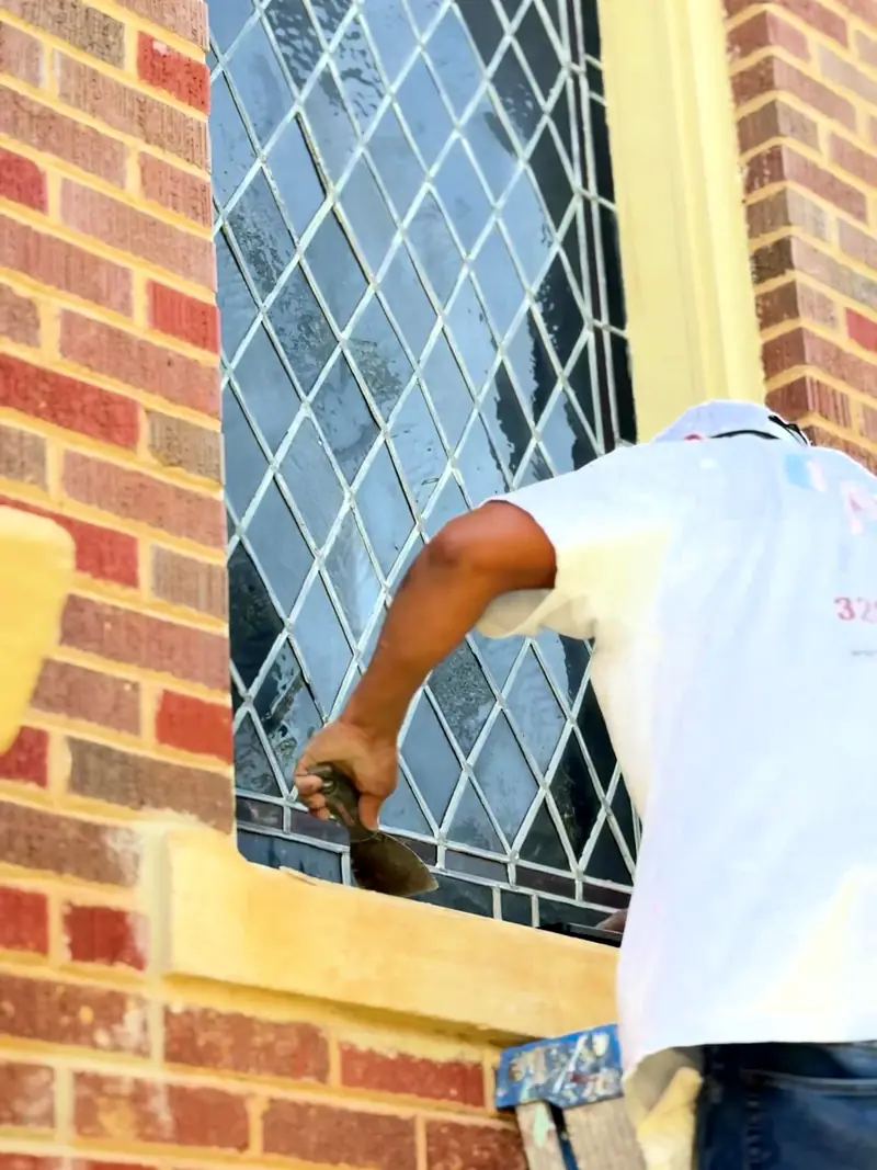 Alvarez Painting crew member preparing window trim on a brick home